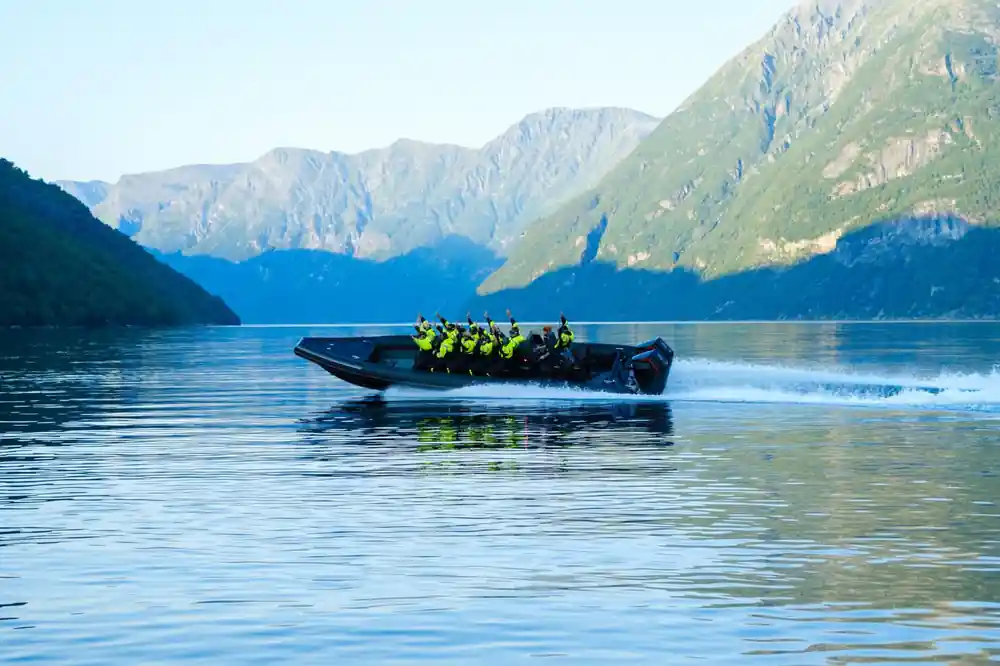 The boat crossing glassy water under a green mountain