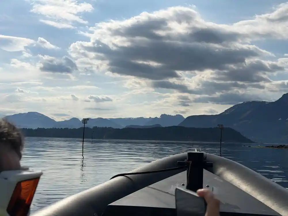 The bow rail and a bright cloudy sky over the fjord