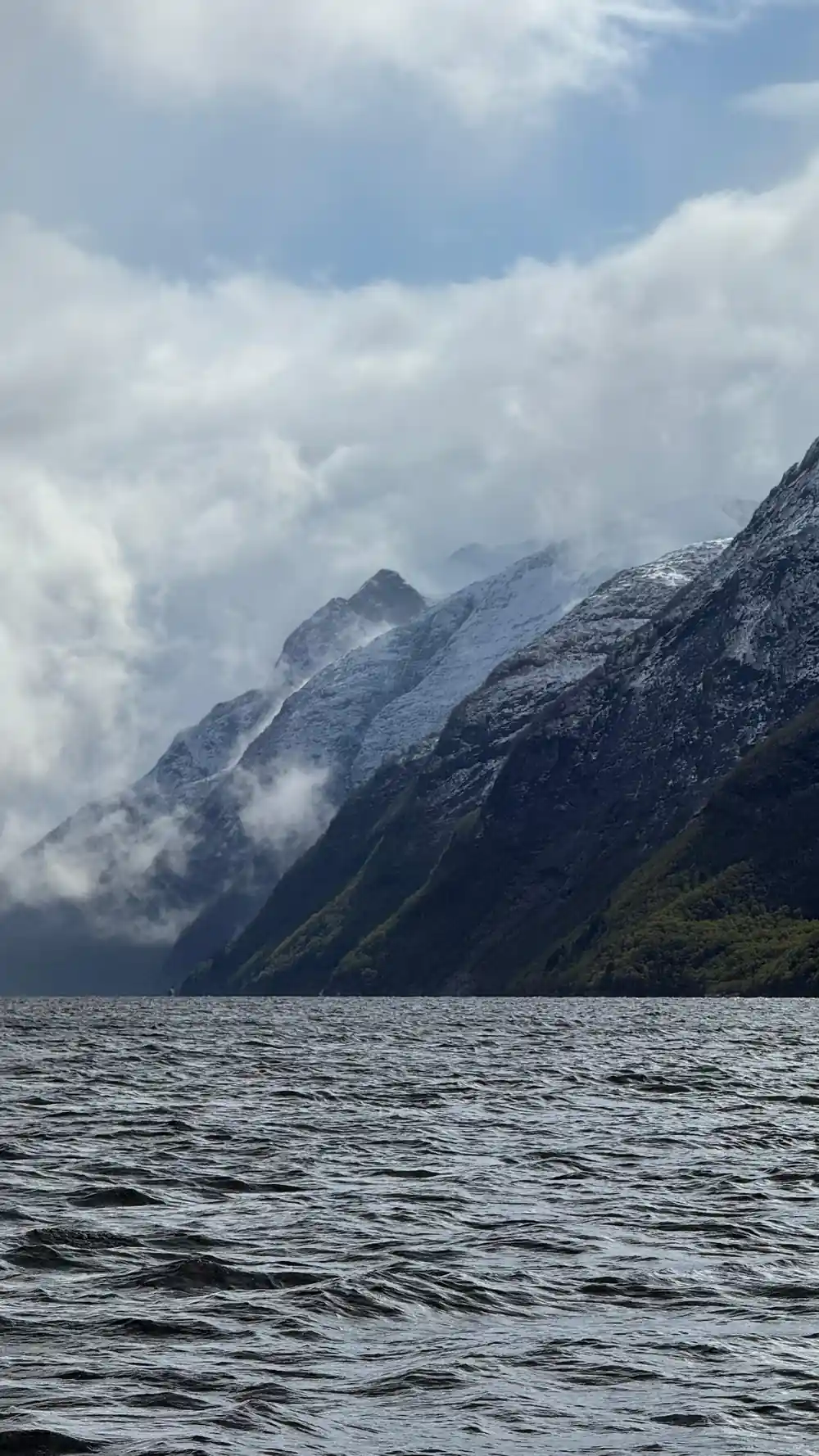 Cloud sitting on a snow-covered ridge above grey water