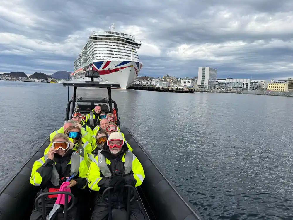 Group in yellow flotation suits aboard the RIB with a cruise ship behind