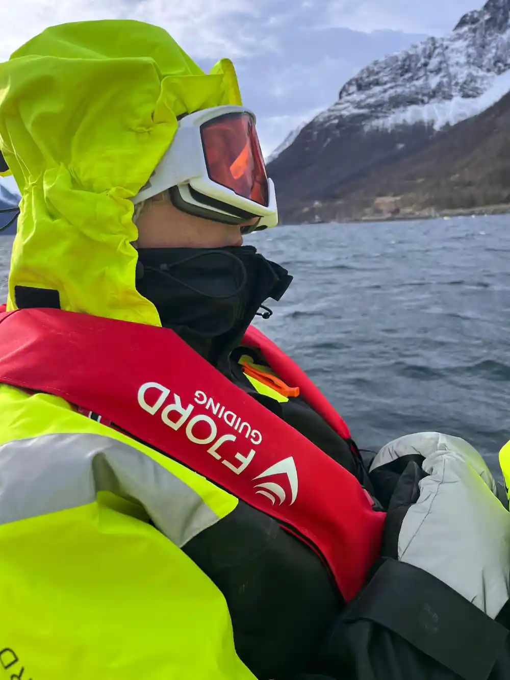 A passenger in a suit and goggles beside the fjord wall