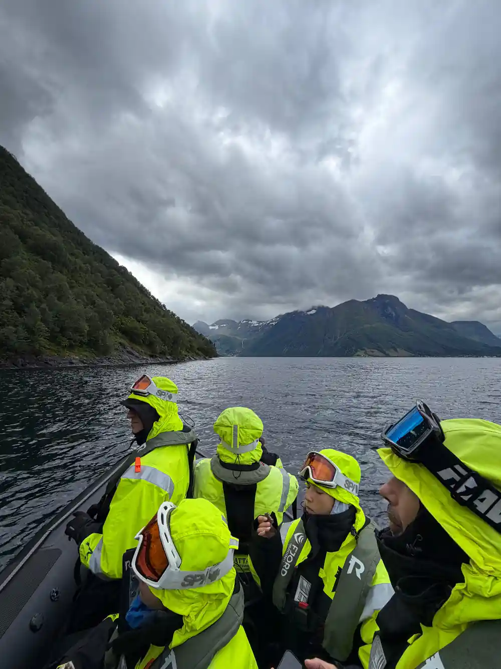 Passengers seated low in the boat under a dark ridge