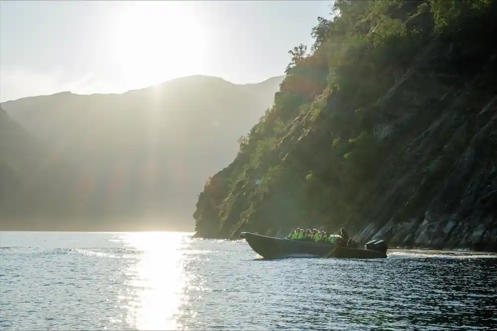 The RIB silhouetted against sun on the water below a cliff