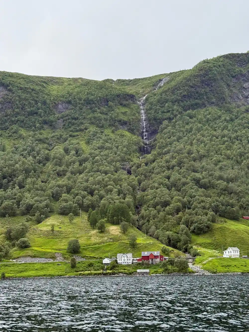 A waterfall and white farmhouse on a green mountainside